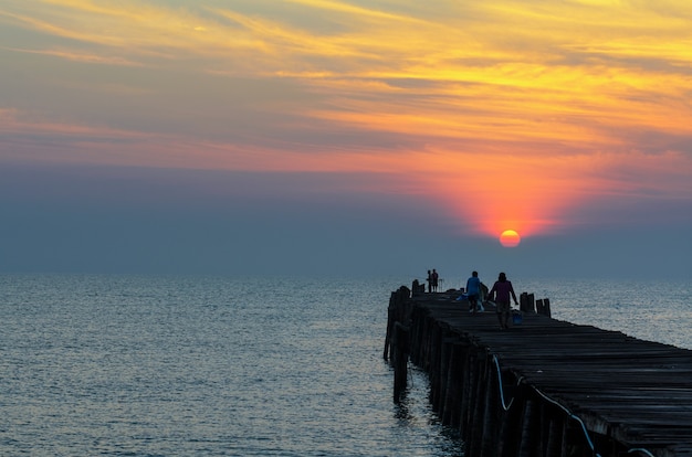 Silhouette fisherman on the old wooden bridge and sea at sunrise in rural Thailand.