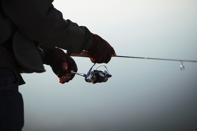 Siluetta della canna da pesca della tenuta della mano di un pescatore