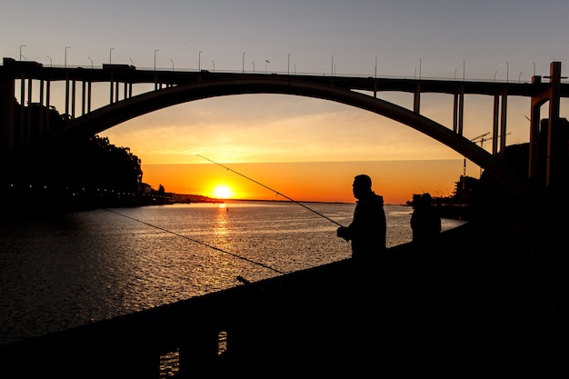 Silhouette of fisherman over sunset in the city.