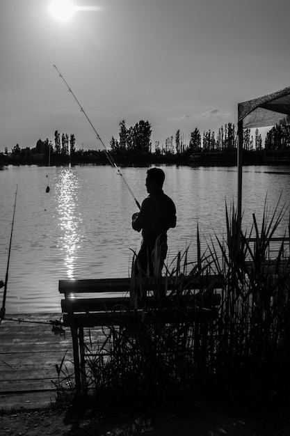 Silhouette of a fisherman with a fishing rod on the background of the lake