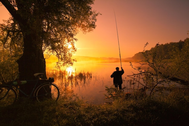 Silhouette of fisherman with fishing rod on the lake at sunset