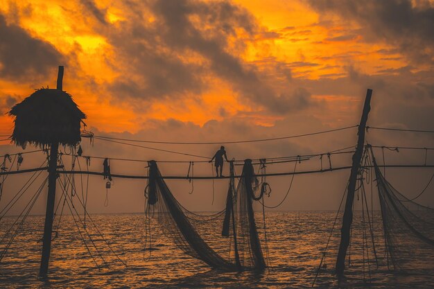 Photo silhouette of fishermen casting a nets on fishing poles on sunrise traditional fishermen prepare the fishing net local people call it is day hang khoi fisheries and everyday life concept