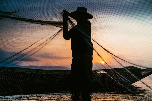 Foto sagoma di pescatori utilizzando strumenti di pesca e durante il sole dorato splende