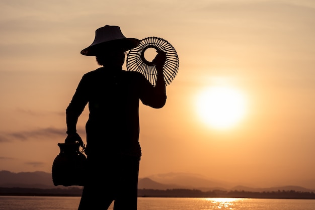 Foto sagoma di pescatori utilizzando strumenti di pesca e durante il sole dorato splende