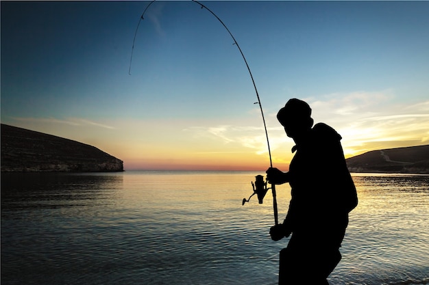 夕日の海の海岸で釣り人のシルエット