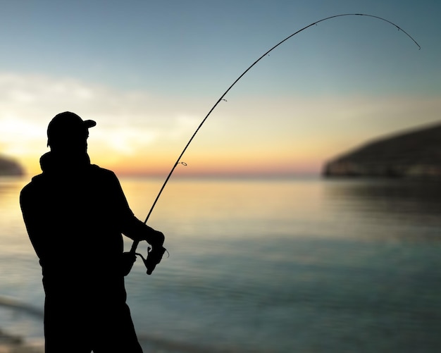 Silhouette of fishing man on coast of sunset sea