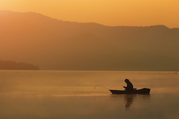 Silhouette uomo di pesca seduto e guarda smart phone