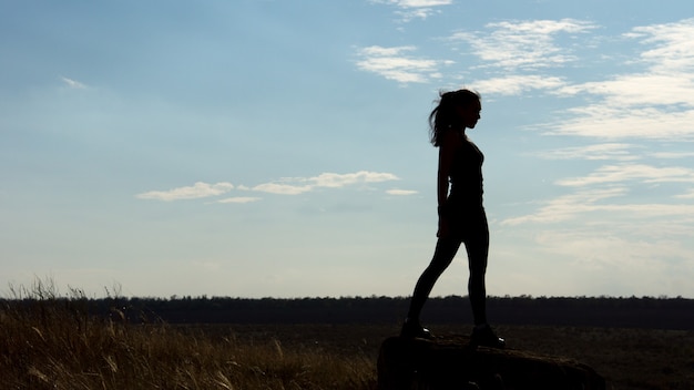 Silhouette of a fit healthy sexy woman standing on the horizon against a late afternoon sky