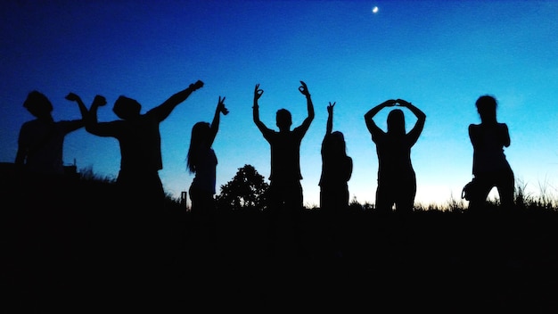 写真 夕暮れの空に逆らってフィールドで踊るシルエットの友達