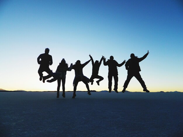 写真 夕暮れの晴れた空に砂の上をジャンプするシルエットの友達