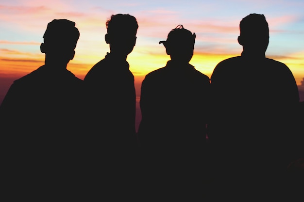 Фото Силуэт друзей, стоящих на небе во время захода солнца.