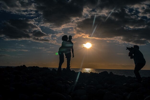 写真 夕暮れの間雲の空を背景にビーチに立っているシルエットの友達