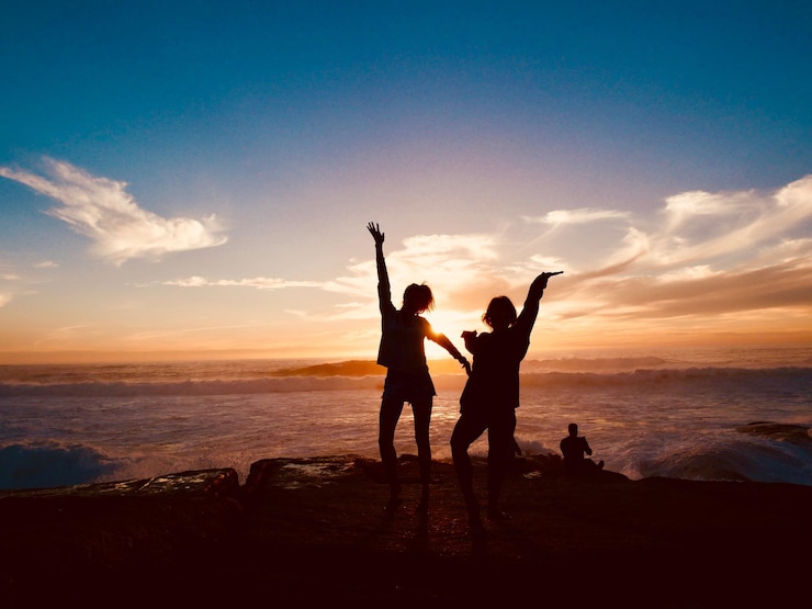 Photo silhouette friends standing at beach against sky during sunset