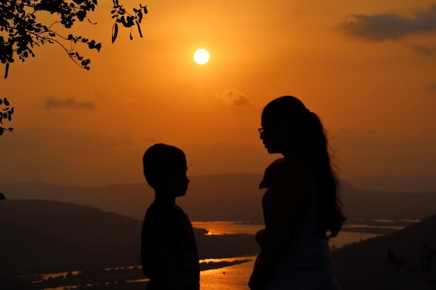 Silhouette friends standing on hill against orange sky during sunset