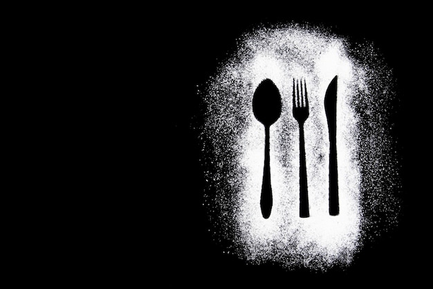 Silhouette from a knife, fork, and spoon sprinkled with flour on a dark background with copy space