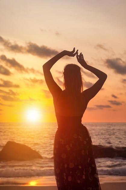 Silhouette from behind pretty woman with arms raised relaxing on ocean beach at sunset background Lady on sea beach in summer vacation