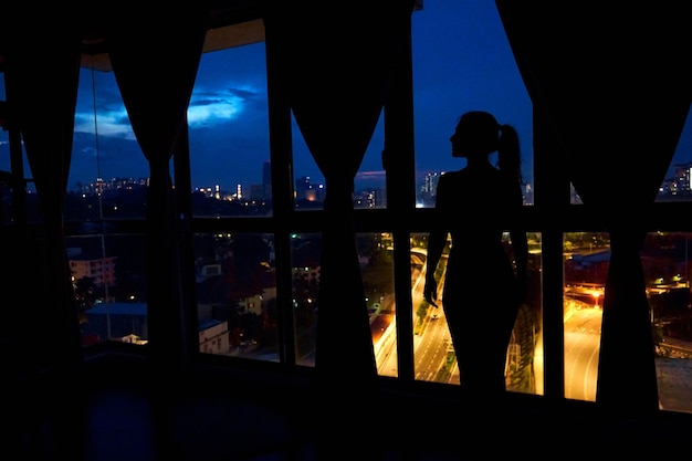 La silhouette di una ragazza contro una vetrata guarda la città di notte