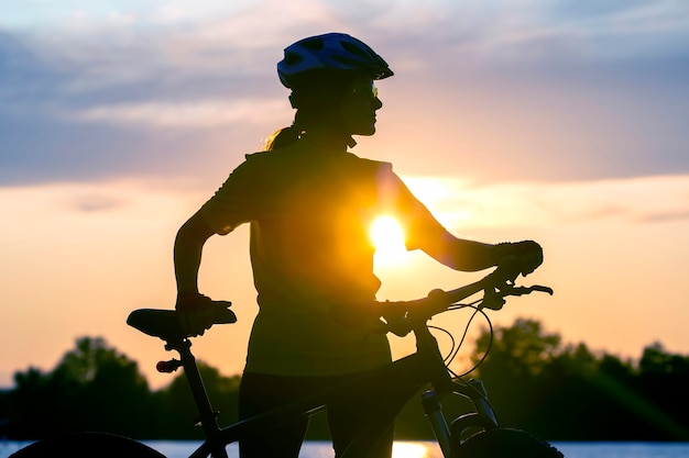 Silhouette of a girl cyclist with a bicycle on the background of a sunset sky. Healthy lifestyle and sport. Leisure and hobbies