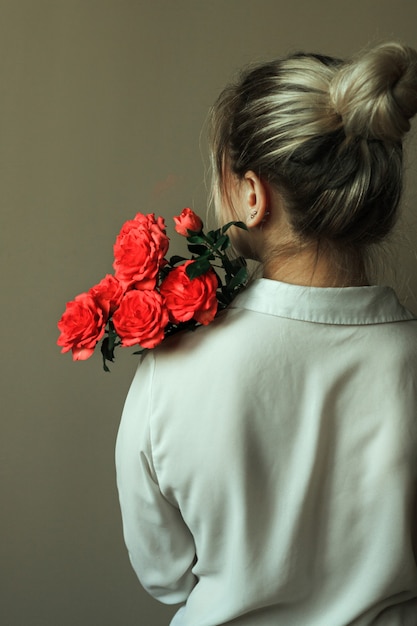 Silhouette of a girl from the back with gathered hair in a bun and a blouse with a bouquet of roses.