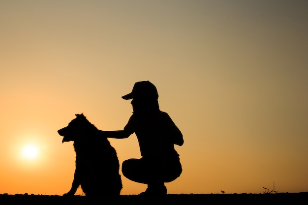 女の子と美しい夕日の背景と彼女の犬のシルエット。