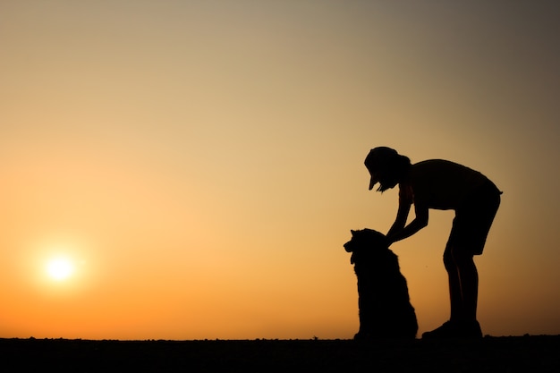 女の子と美しい夕日の背景と彼女の犬のシルエット。