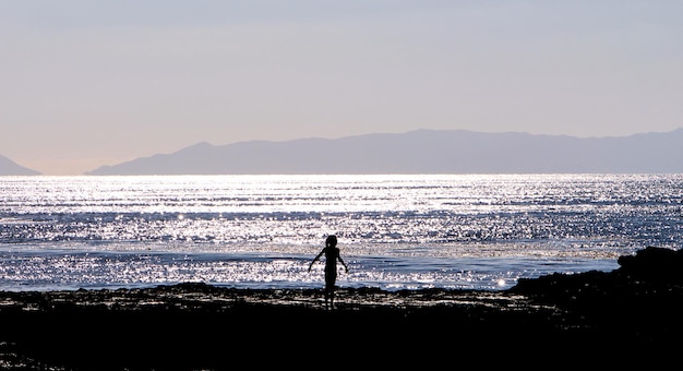 晴れた日に空の向こうのビーチに立っているシルエットの女の子