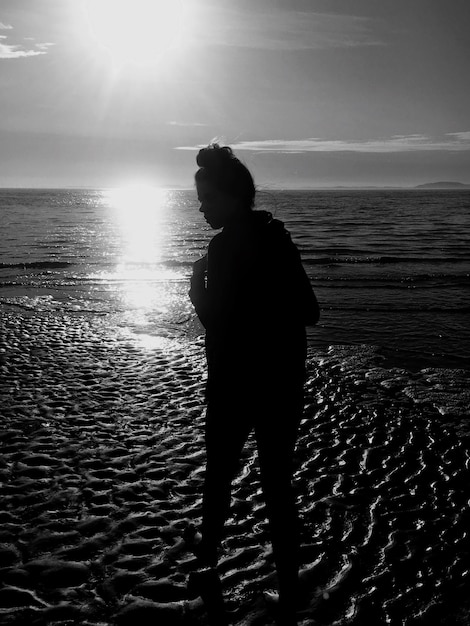 Foto ragazza a silhouette in piedi sulla spiaggia contro il cielo