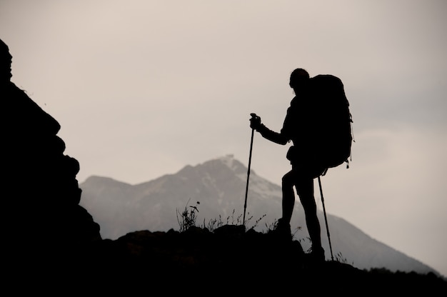 Silhouette girl standing on the rock with hiking backpack and walking sticks