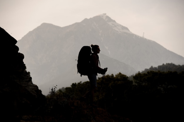 Silhouette girl walking on the rock with hiking backpack and sticks