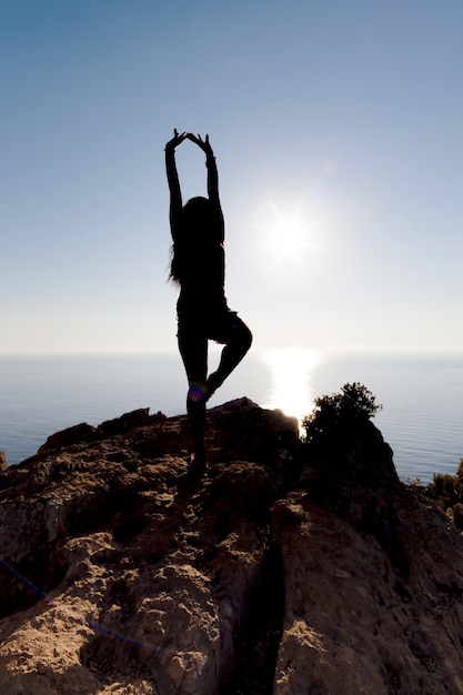 Siluetta di una ragazza che è impegnata nello yoga sulla collina sul mare e al tramonto, lo stato di libertà
