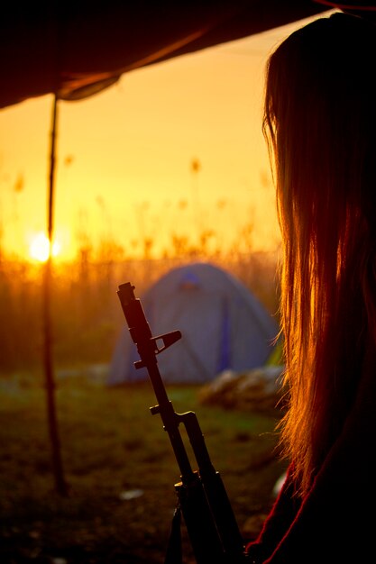 Photo silhouette of a girl with a gun in his hands on the background of the sunrise