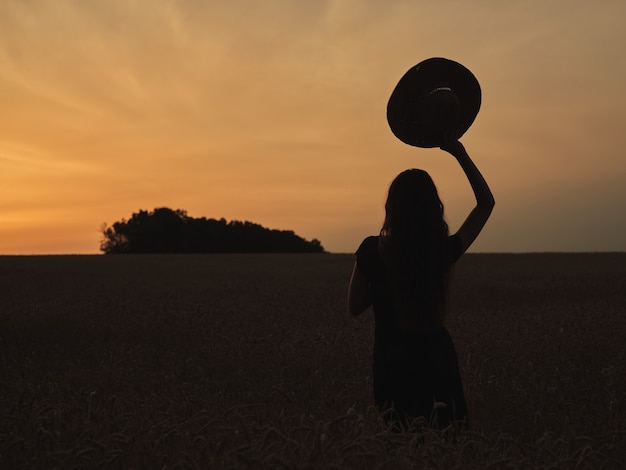 Silhouette of a girl with a hat in a field at sunset