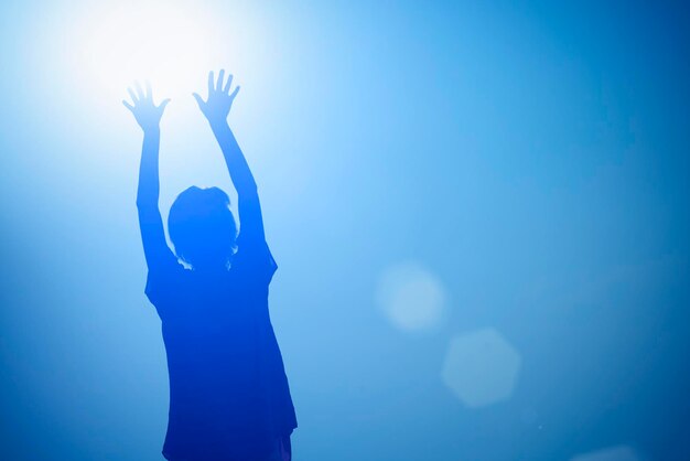 Silhouette of a girl with raised hands to the sun on a blue background