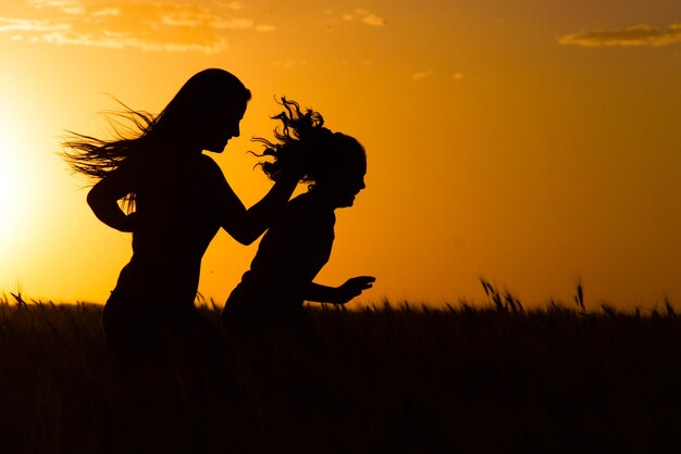 Foto silhouette di ragazze che corrono sul campo contro il cielo durante il tramonto