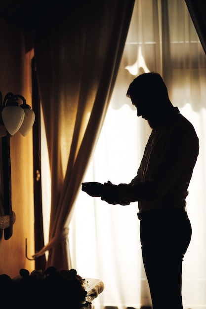 Silhouette of the groom getting dressed in the room