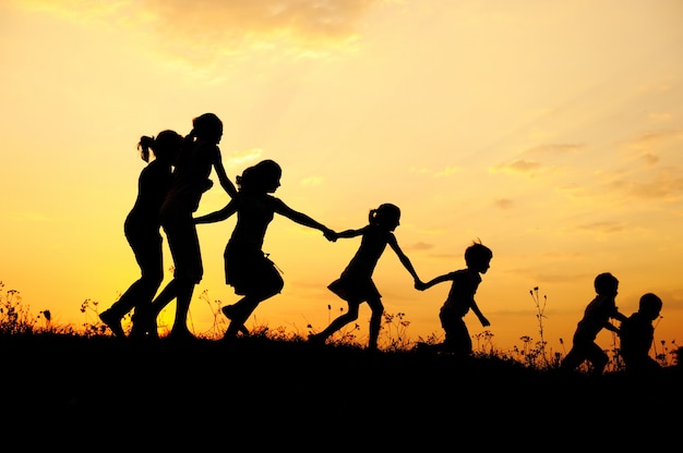 Silhouette, group of happy children playing on meadow, sunset, summertime