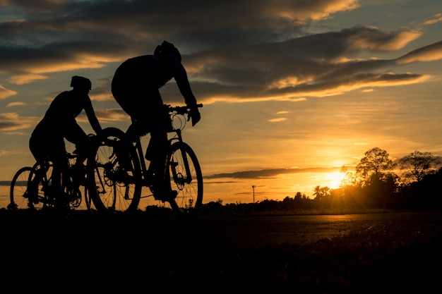 Silhouette group of men riding bicycle at sunset.