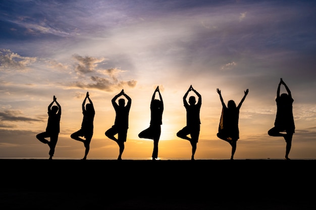 Silhouette of group of people doing yoga during colorful sunset or sunrise at a beach