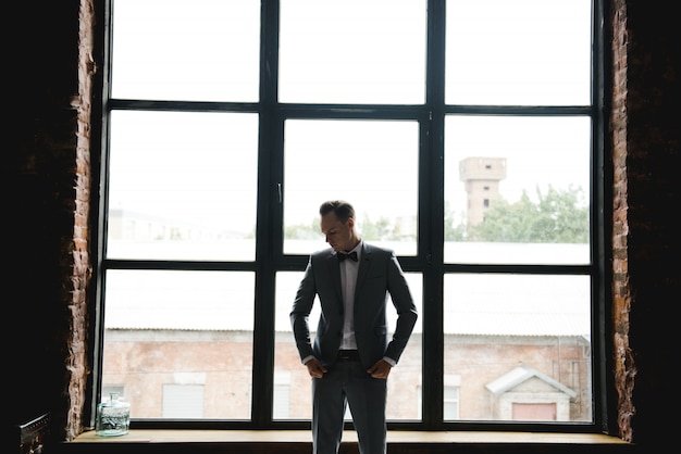 Silhouette of the guy in front of the window. Morning of the groom. Room in loft style. Big windows.