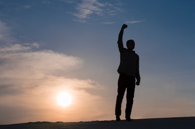 Photo silhouette of guy with hands up at sunset time on sky