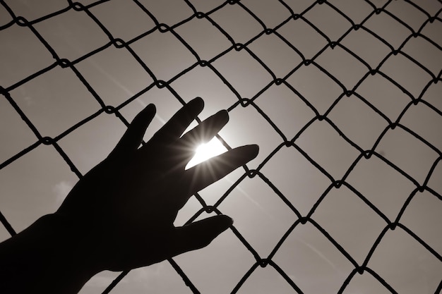 Silhouette hand and fence on sky background Concept of hurdles and hopes