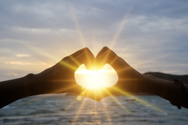 Foto profili la mano nella forma del cuore con alba sui precedenti della spiaggia