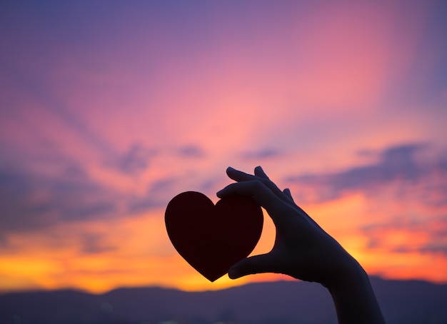 Silhouette hand holding beautiful heart during sunset background. 