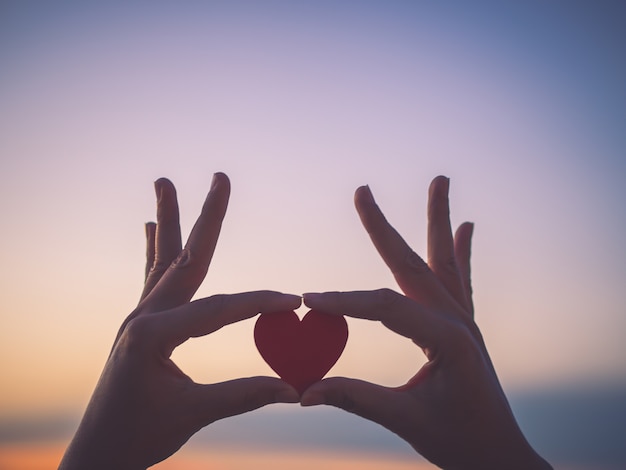 Silhouette hand holding beautiful heart during sunset background.