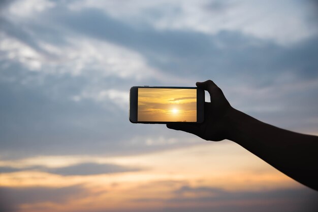 Silhouette hand holding smartphone take photo in the sunset.