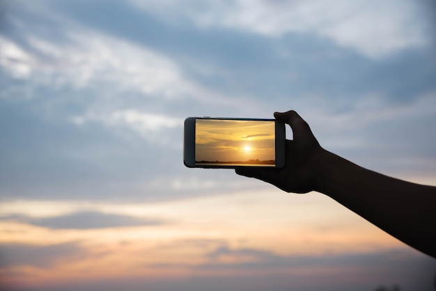 Silhouette hand holding smartphone take photo in the sunset.