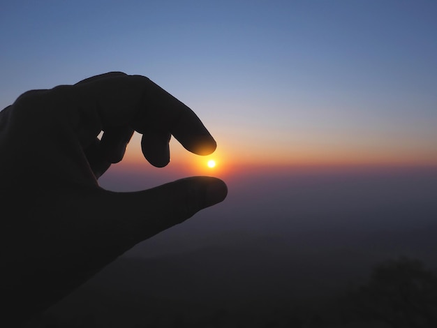 Foto silhouette di una mano che raccoglie il sole all'alba