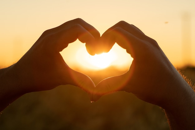 The silhouette of a hand in the shape of a love heart at sunset hands forming a heart shape with sun...