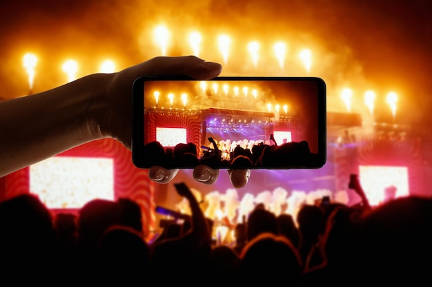 Silhouette of hand using camera phone to take pictures and videos at pop concert festival