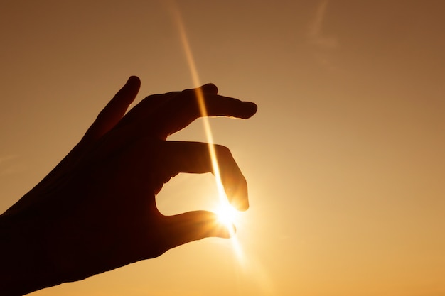 일몰에 대 한 손의 실루엣입니다. 손가락 사이의 광선으로 태양.